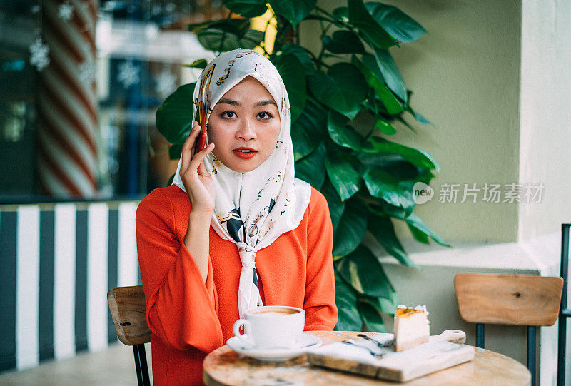美丽的亚洲穆斯林女人在咖啡馆和她的智能手机