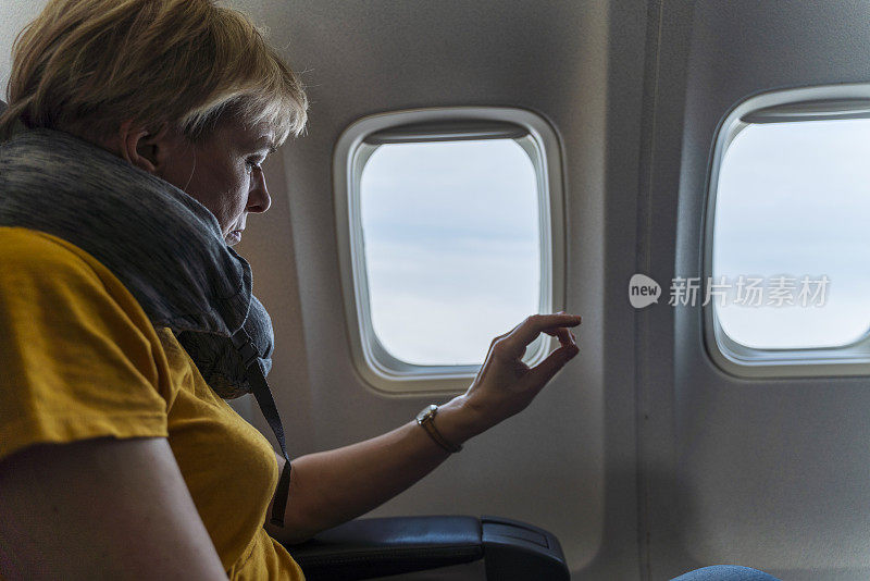 55岁的成熟女性在飞机上望向窗外的云彩。