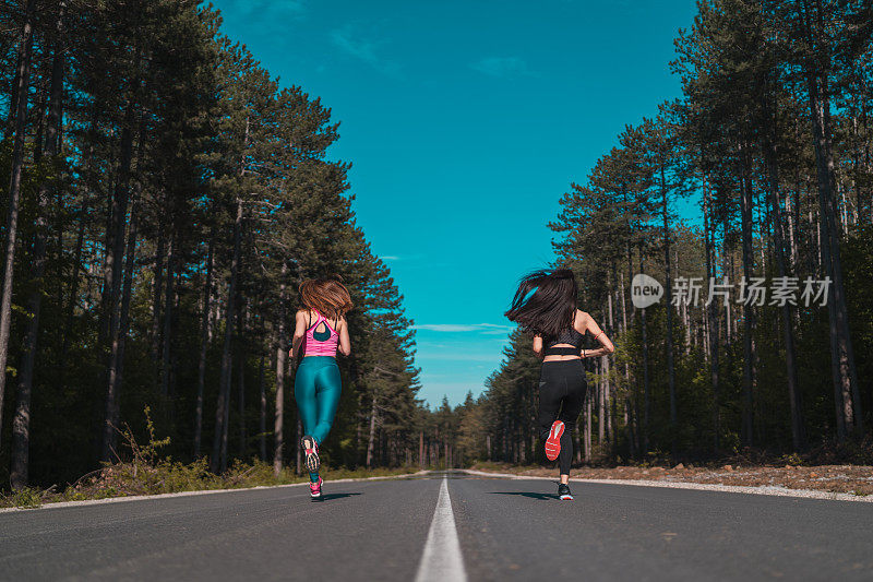 两个女孩在公园的柏油路上奔跑的背影