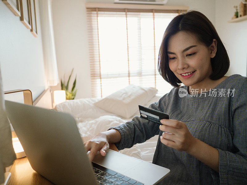 年轻女子在家里放松的时候使用笔记本电脑和信用卡