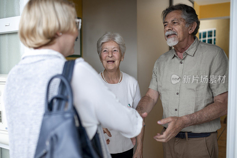 一对老年夫妇打开前门，迎接一名女性保健工作者进行家庭健康访问