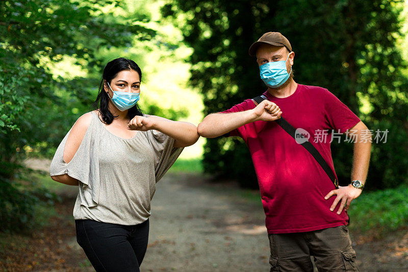 戴着防护口罩的朋友们在公园户外进行2019冠状病毒病肘撞