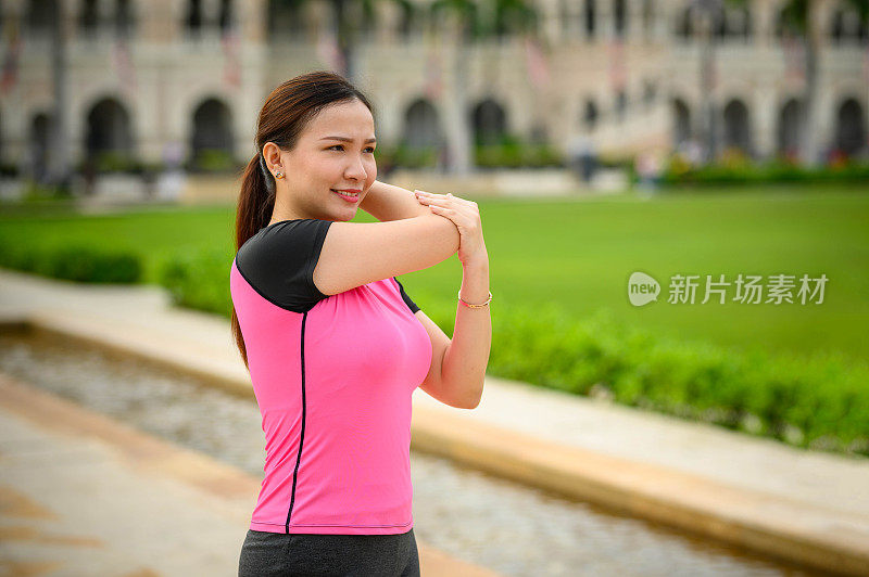 一位穿着运动服的亚洲妇女在户外人行道上运动时热身和伸展