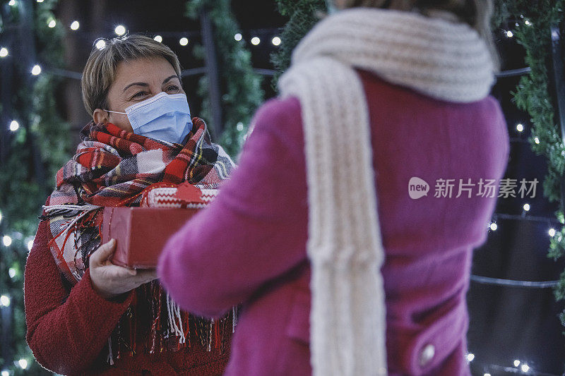 一个戴着防护面具的成熟女人给她的小女儿送圣诞礼物