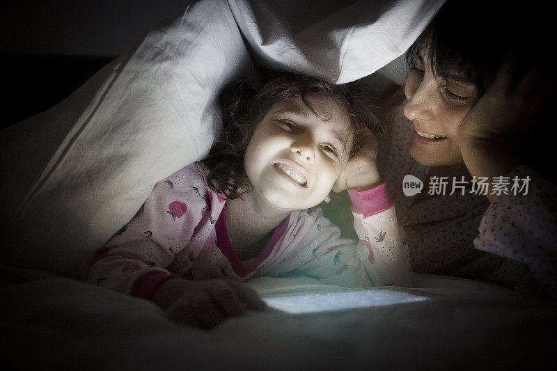 快乐的妈妈和女儿在毯子下看卡通