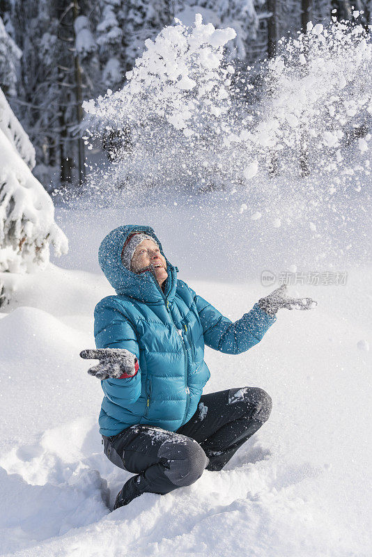 在冬天的森林里，成熟的女人穿着皮大衣向空中抛雪