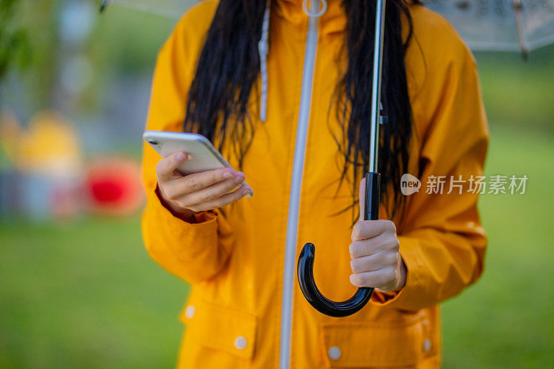 上腹部的女人在黄色雨衣与雨伞使用电话