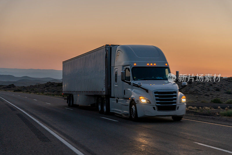 一辆商业货运卡车在沙漠公路上向东驶去，一个戏剧性的日落背景