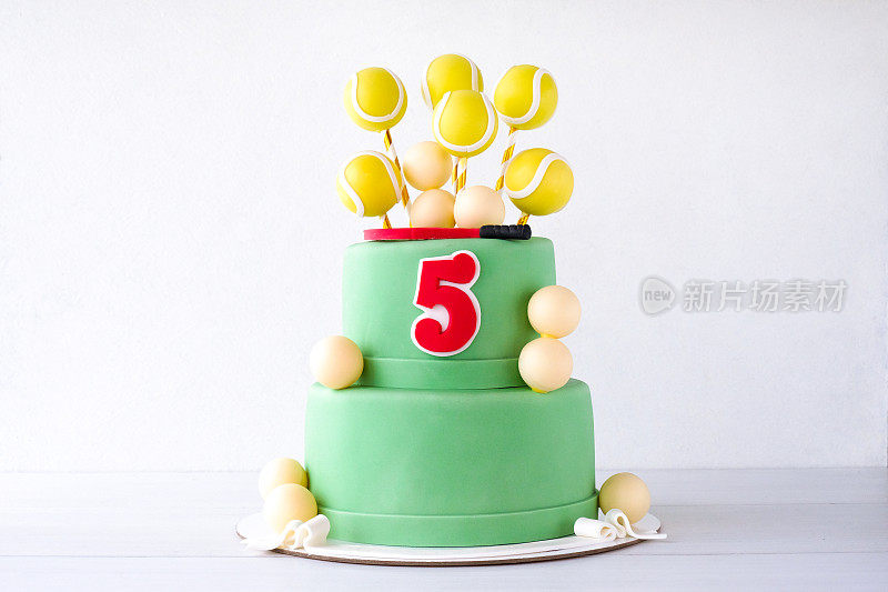 用黄色的球和球拍装饰的绿色双层网球生日蛋糕