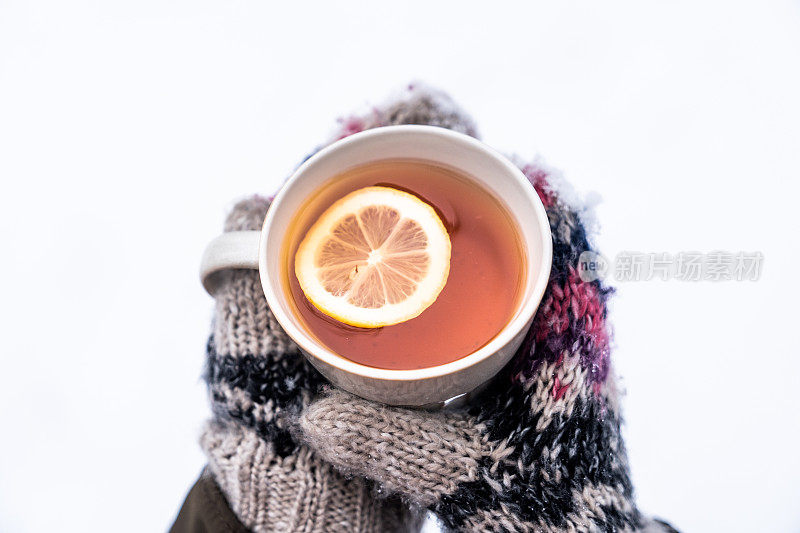 手戴针织手套，拿着一杯柠檬热茶。