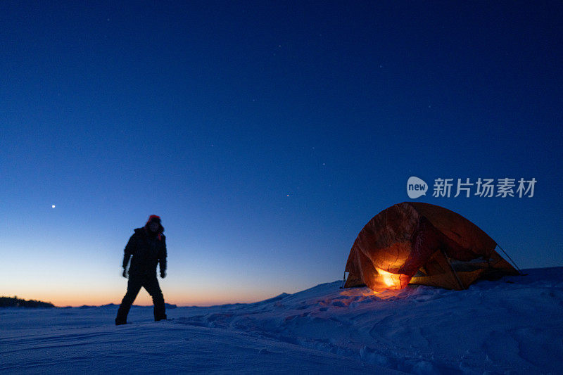 男子望向冰雪覆盖的雪地，背景是露营的帐篷