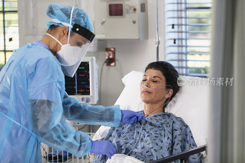 穿着个人防护装备的护士给病床上的病人供氧