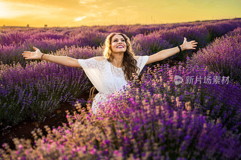 穿着白色连衣裙的女人在夕阳下走过薰衣草田