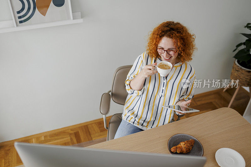 年轻女子喝着咖啡，吃着羊角面包，在办公室查收邮件