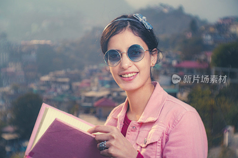 自信、快乐的年轻女子拿着一本书看着镜头。