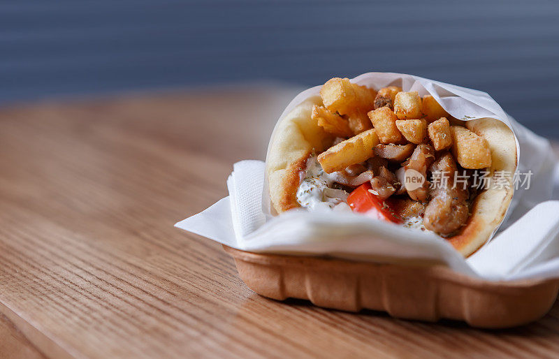 希腊羊肉串肉裹在皮塔饼里，配上薯条和白酸奶酱，装在一次性纸盘里带走