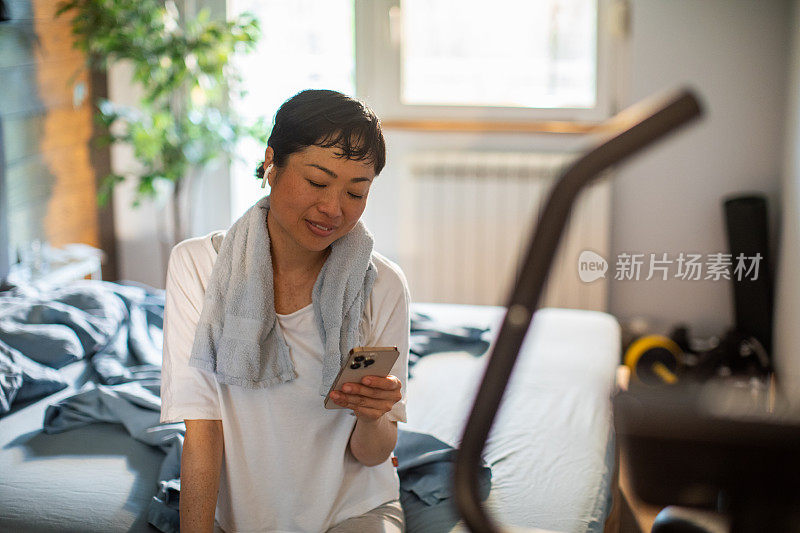 年轻的日本女子在家里锻炼完后使用智能手机