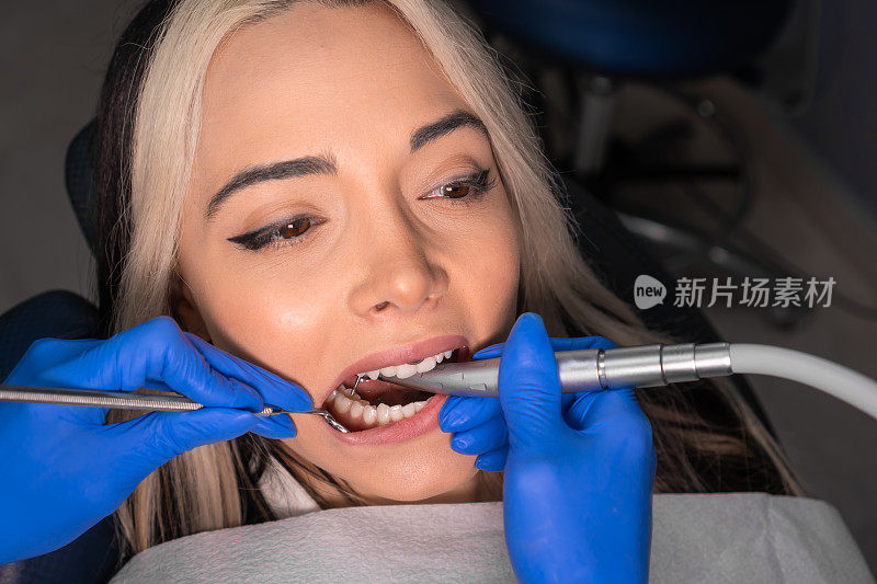 牙医正在给一位年轻女子治疗牙齿。一位美丽的年轻女子坐在牙医的椅子上接受牙科治疗。现代牙科技术