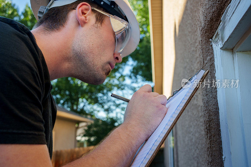 年轻的白人检查员检查、记录并拍摄了一栋现代灰泥房屋外的户外门框