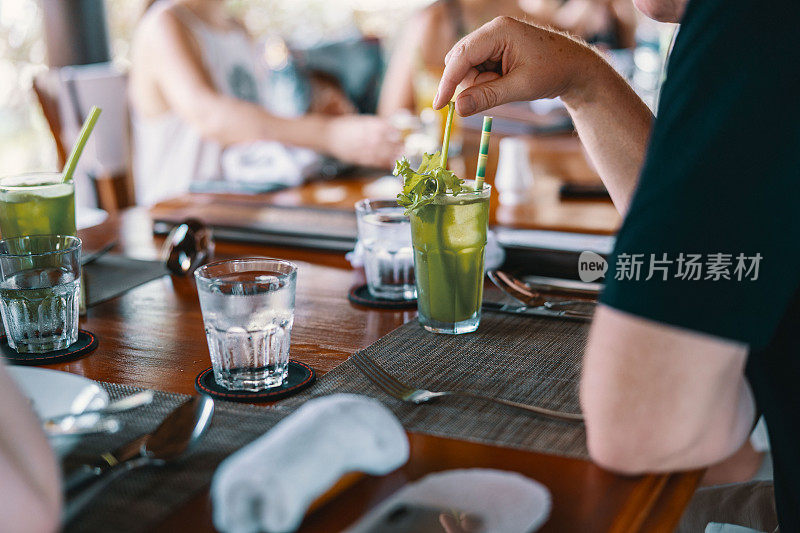 等待用餐的男子端着绿色鸡尾酒在餐桌上