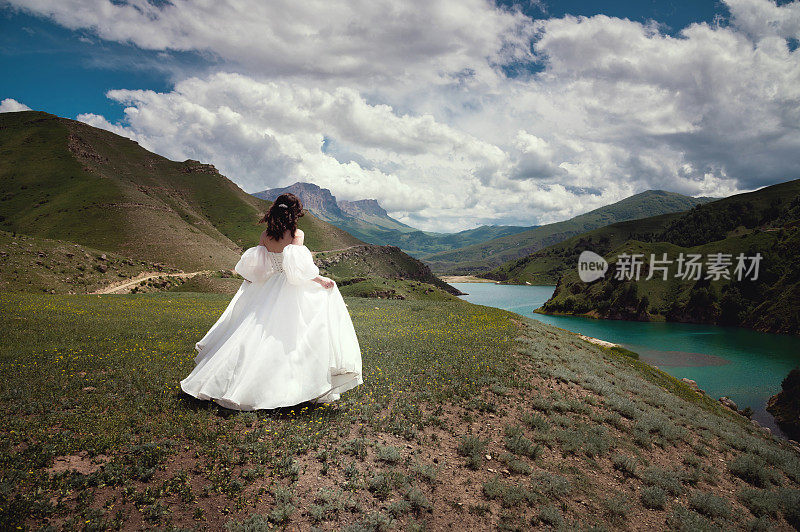 一个美丽的新娘的后景，女人在山上的草地上奔跑，风吹着她的婚纱。自然景观