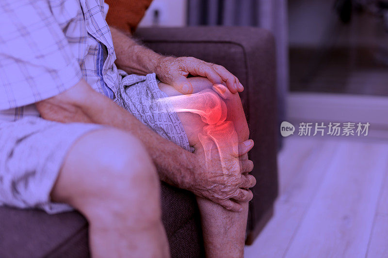 一位老人坐在家里客厅的沙发上按摩膝盖，腿部疼痛