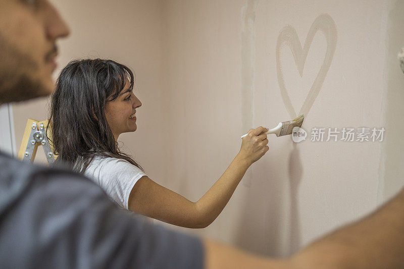 男人用油漆滚筒在墙上画画，而他的女朋友在墙上写着心。