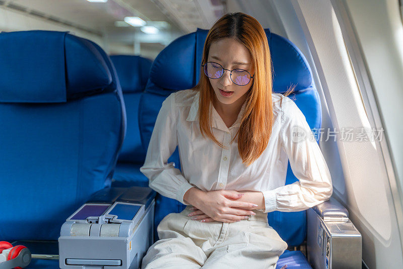 一名年轻女子坐在飞机上的座位上，用手捂着肚子，试图缓解疼痛
