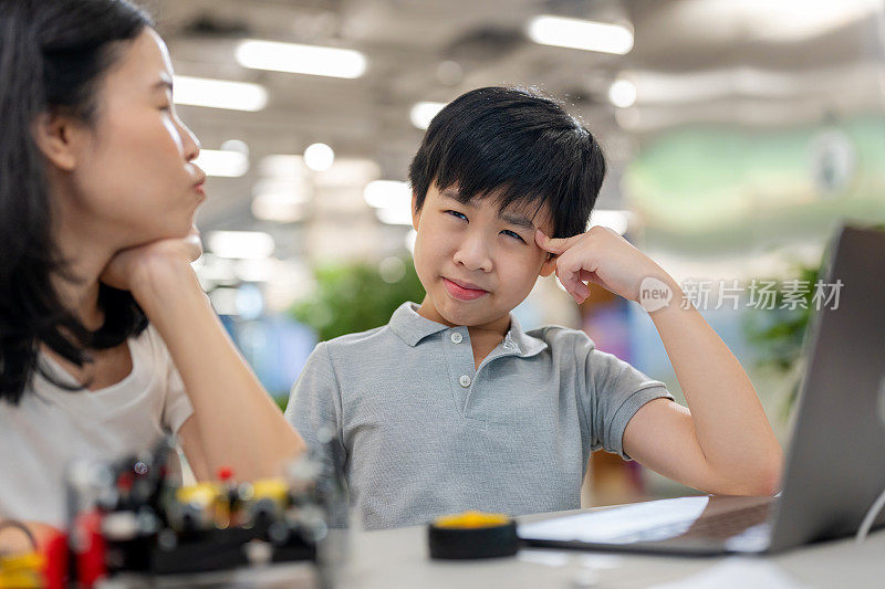 一个年轻的亚洲男孩全神贯注地学习STEM教育培训课程，专心地建造和修理机器人原型。坐在摆满电子元件、文书和电脑的办公桌前，象征着发展和创新。