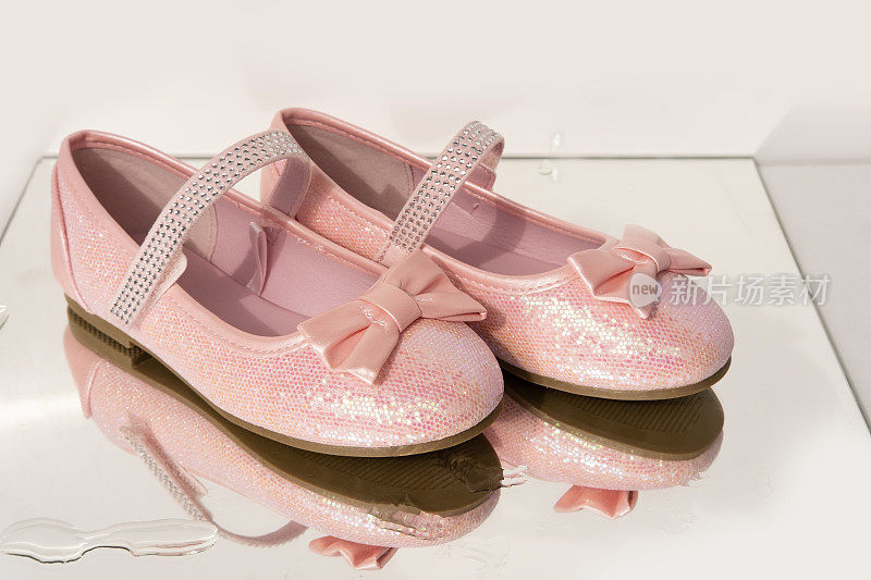 一双漂亮的粉色正装鞋，上面有蝴蝶结和闪闪发光的小公主，在湿镜子上有水滴的背景，快乐的童年，时尚的粉色套装适合特殊场合