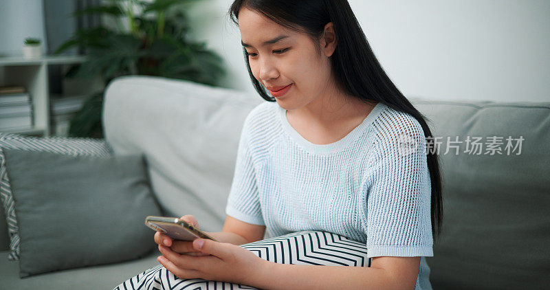 年轻女子在家里的沙发上玩手机。