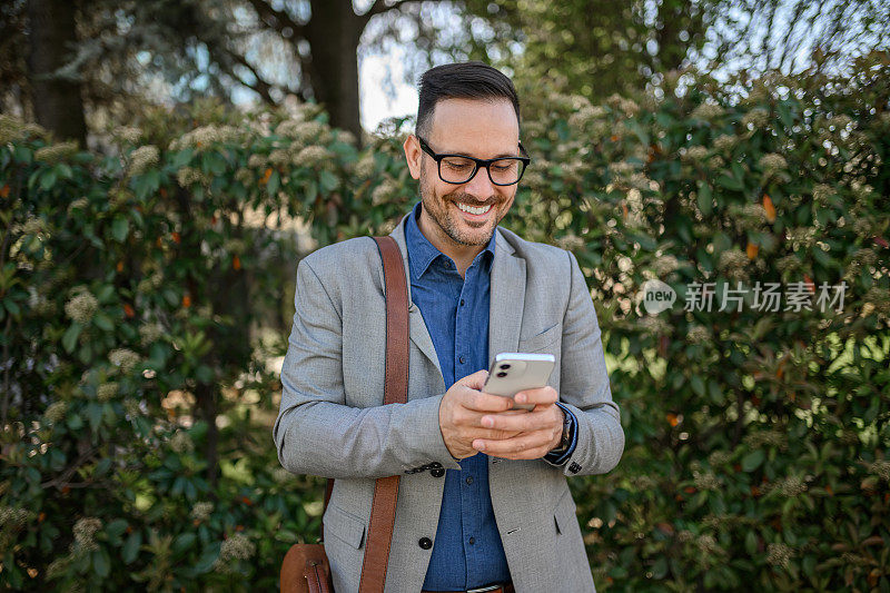 帅气的专业人士，戴着眼镜，背着包，用手机在网上发短信反对植物