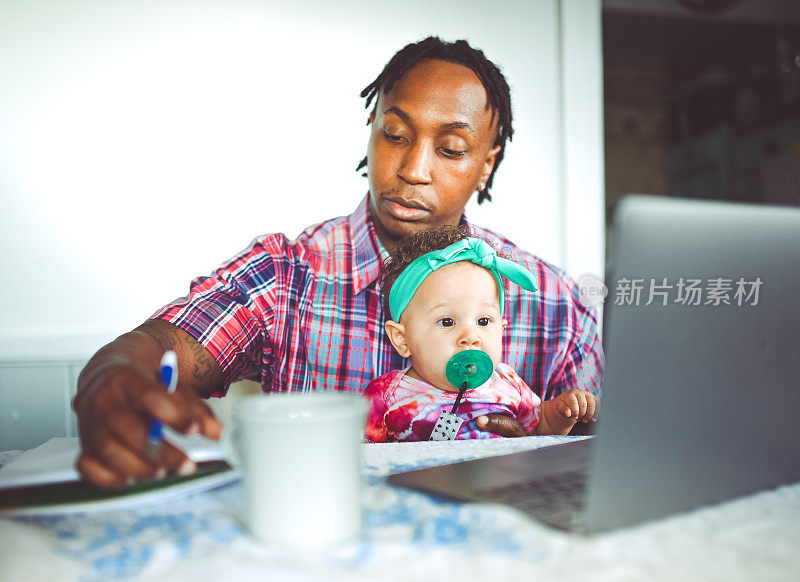 非裔美国人的父亲在电脑上工作和他的婴儿女儿在家工作现代男子气概