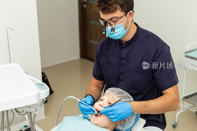 一个男孩戴着手套和显微镜眼镜，让口腔医生给他的牙齿钻孔