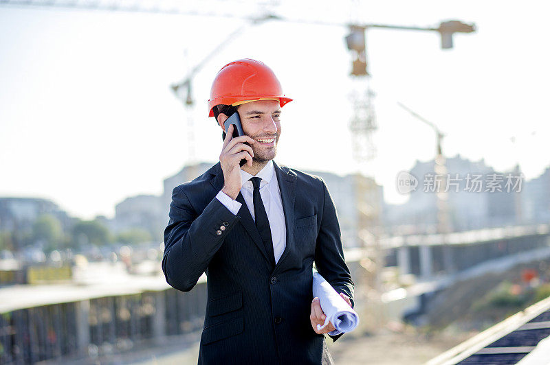 年轻的建筑工程师与项目和安全帽使用电话
