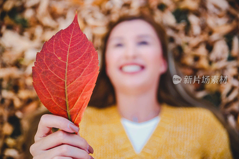 女人在秋天的公园里，拿着一片树叶