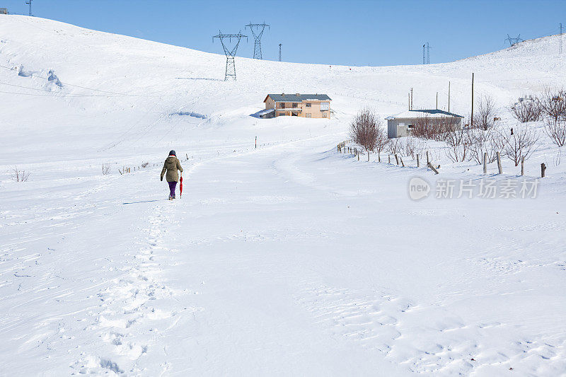 成年妇女穿着暖和的衣服在雪地上行走在农村