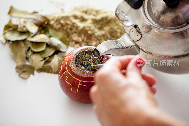 温柔地将热水注入干马黛茶在美丽的葫芦，使传统的巴拉圭茶饮料-储备照片