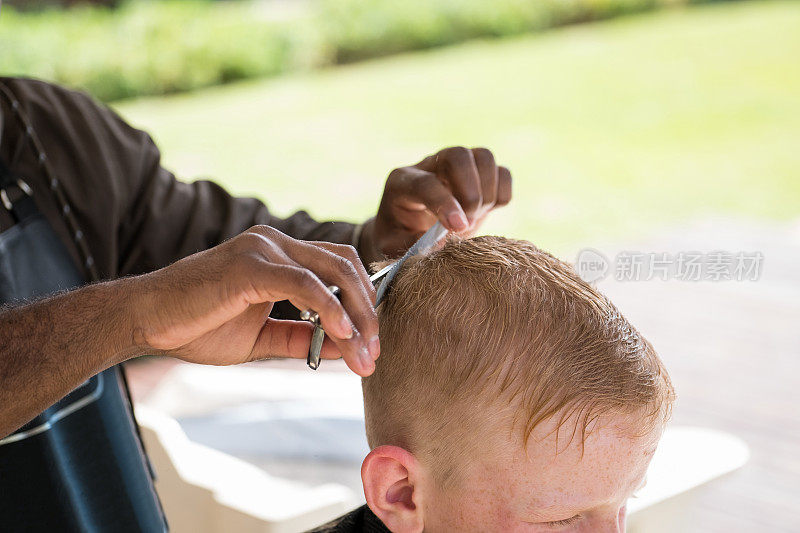 非洲男性理发师正在给一个男孩理发