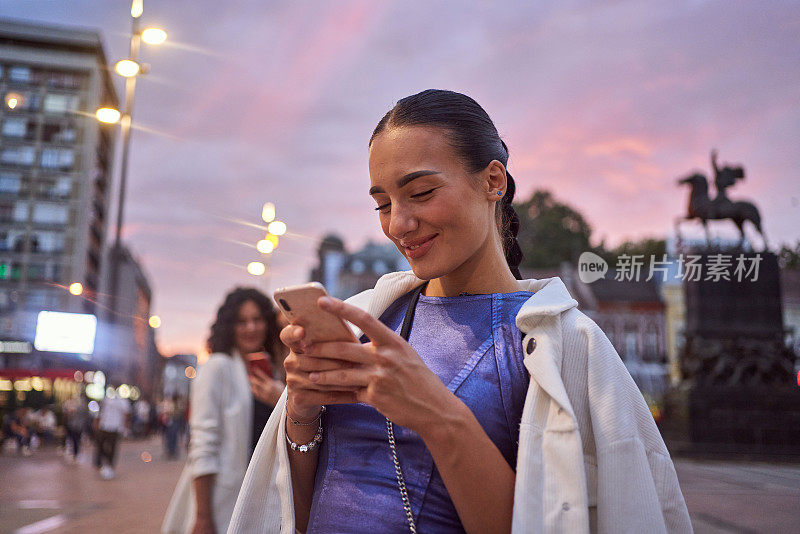 美丽的微笑的女人在爱的手机短信在城市的户外