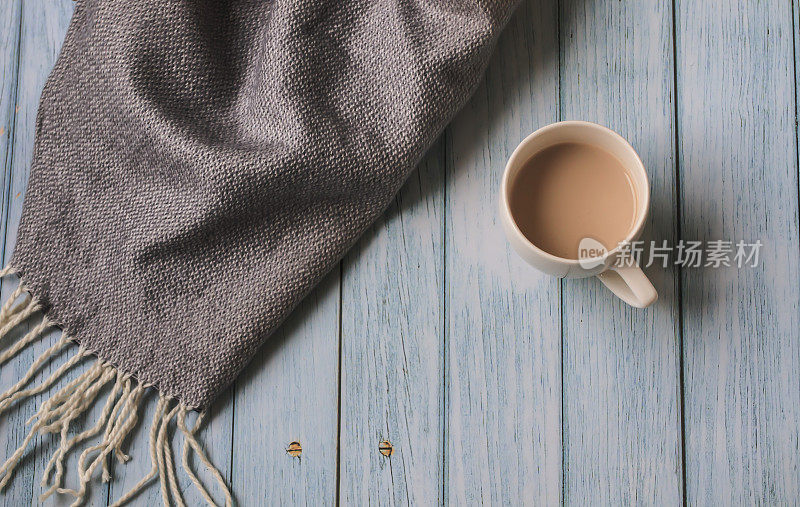 秋天舒适的构图与柔和的灰色围巾，一杯咖啡在蓝色木质背景与复制空间。秋天早晨的概念。网站上的横幅。平的。