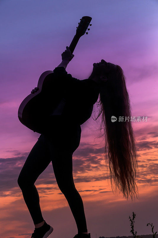 在落日的背景下，一个拿着吉他的女人的剪影