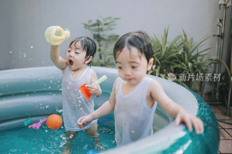 炎炎夏日，一对亚洲华人双胞胎男婴在自家后院的充气游泳池里玩耍