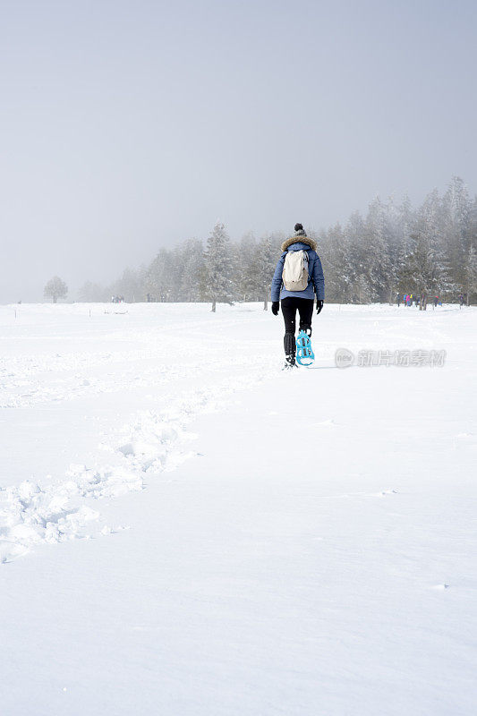 一个女人穿着雪鞋爬上斜坡，在雪地上留下脚印