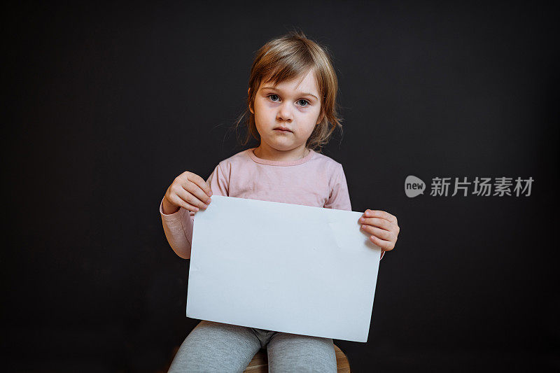 四岁女孩的工作室肖像，带着悲伤的脸拿着空白纸。适合儿童虐待或童工信息