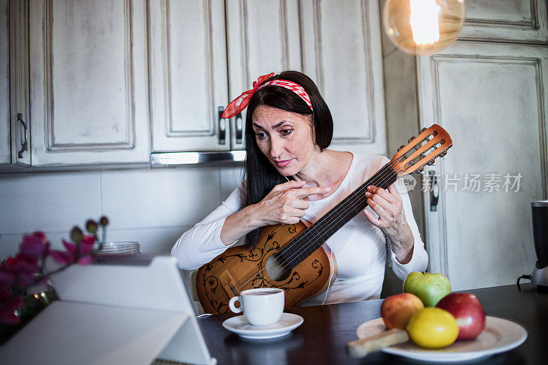 美丽成熟的女人喜欢在厨房里度过清晨，弹吉他，通过平板电脑在线聊天，过着平静的生活。