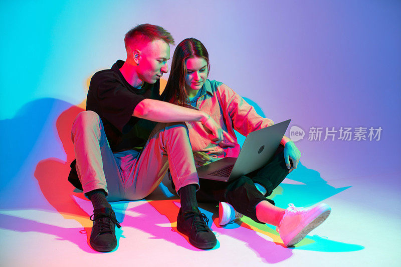 时尚的年轻夫妇用笔记本电脑工作，看电视剧或网上购物。五颜六色的霓虹灯