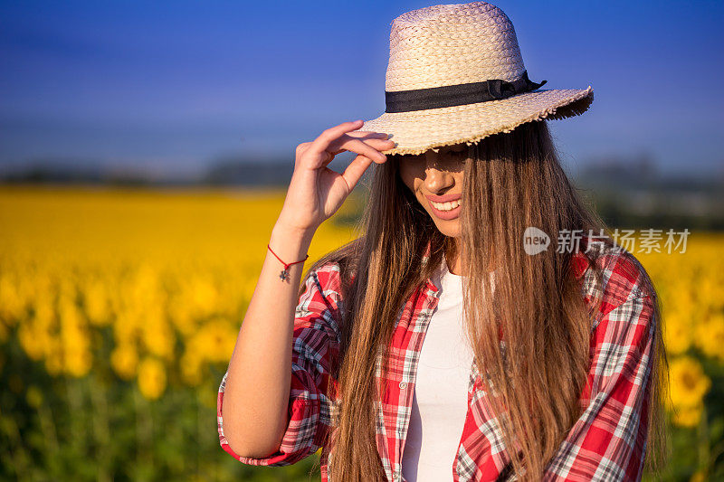 一个美丽的年轻女子的肖像，戴着草帽站在向日葵田