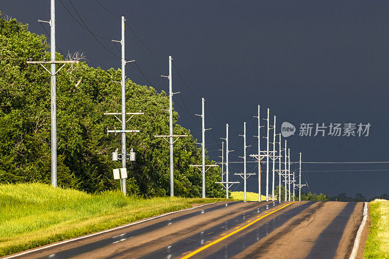 在潮湿的内布拉斯加州高速公路旁的一排银色金属电线杆，背景是黑色的暴风雨云