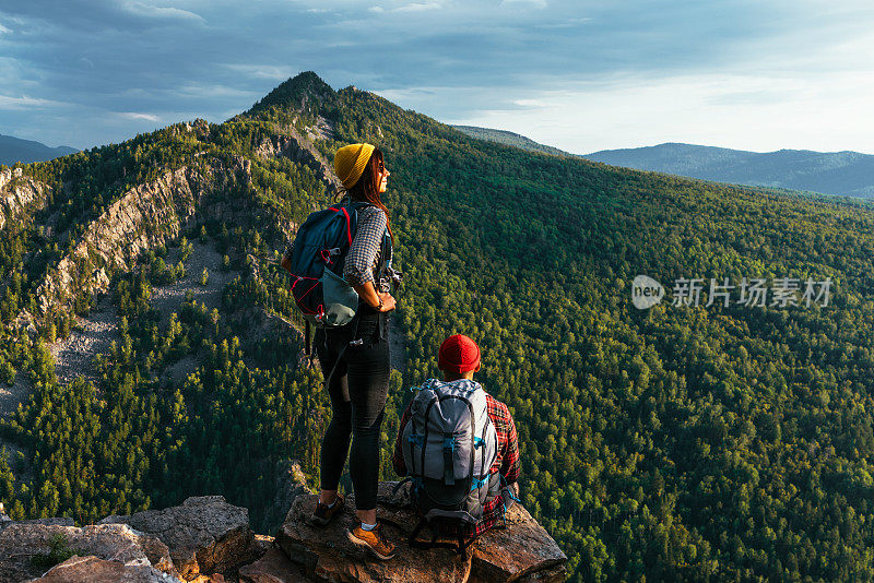 一对幸福的夫妇在山上欣赏美丽的景色。一男一女背着背包在山上欣赏全景。旅行者喜欢在日落时爬山。徒步旅行